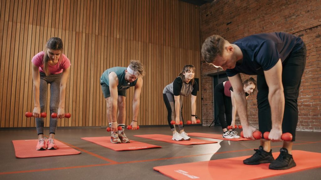 Adults exercising in an indoor fitness class with dumbbells and yoga mats for healthy lifestyle.