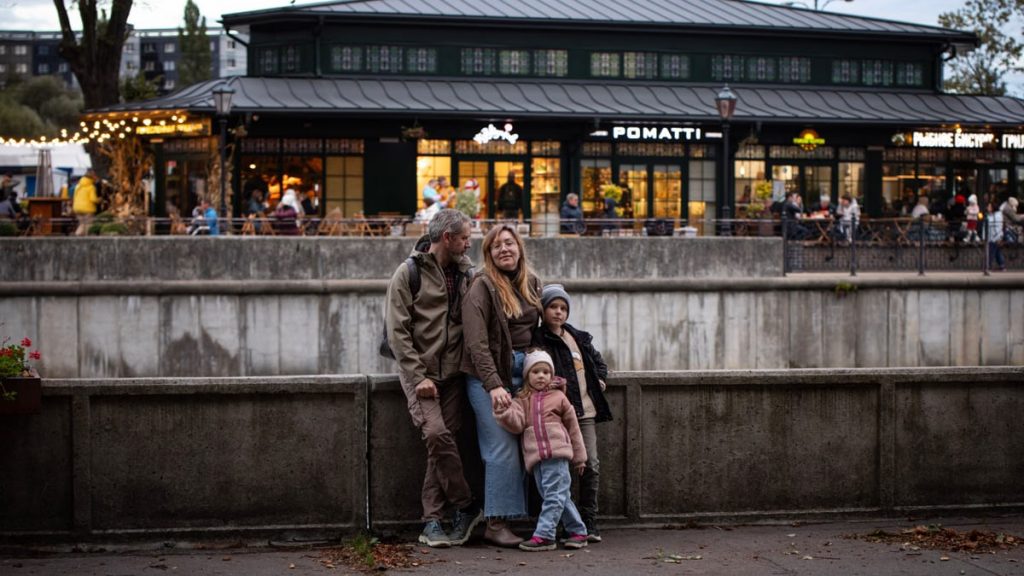 Family of four smiling outdoors in front of a lit café, creating a warm atmosphere in the evening.